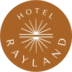 This image shows a brown circular logo with &ldquo;Hotel Rayland&rdquo; written around a stylized sunburst design.