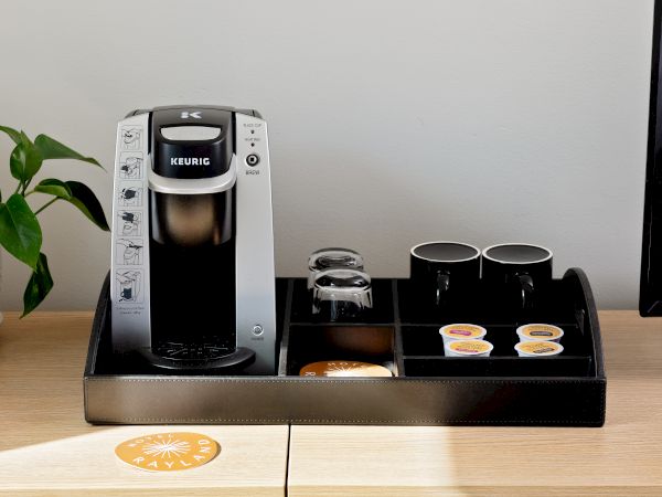 A Keurig coffee maker on a kitchen counter with K-cup pods, a water carafe, and two empty cups, ready to brew.