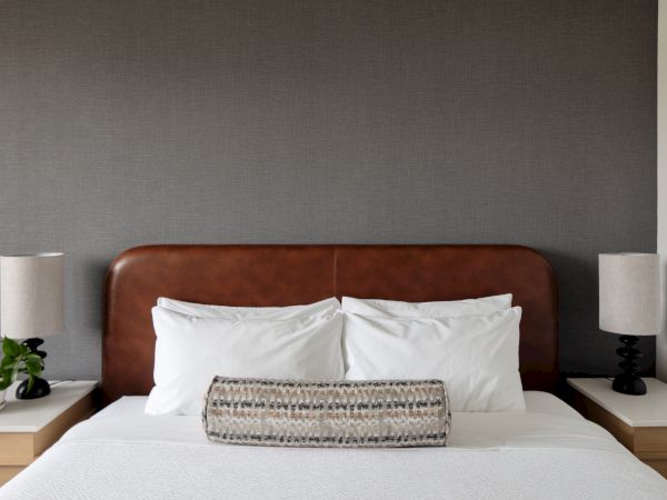 A neatly made bed with white pillows and a patterned throw sits between two bedside lamps against a gray wall, in a calm bedroom.