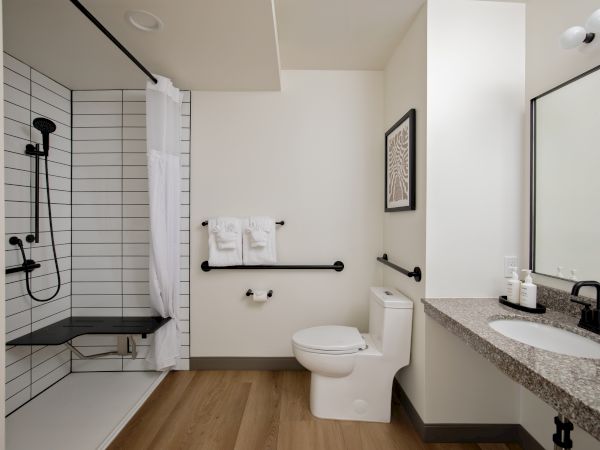 Modern bathroom with a tiled walk-in shower, white curtain, towels, toilet, and granite vanity sink.