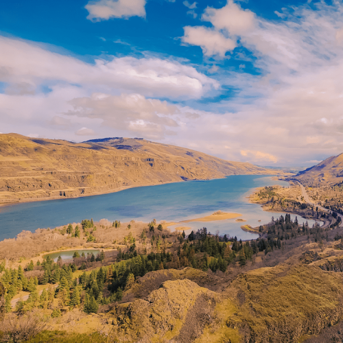 A scenic landscape with a winding river, surrounded by hills and trees under a partly cloudy sky, creating a peaceful natural scene.