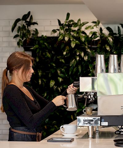 A barista makes espresso at a caf&eacute; machine next to a &ldquo;CAFE&hellip;COFFEEHOUSE&rdquo; logo.