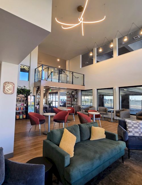 A bright, modern hotel lobby with a seating area of colorful sofas, a wooden floor, high ceilings, and large windows letting in natural light.