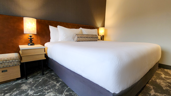 A neatly arranged hotel room with a large bed, two side tables, two lamps, and soft lighting creating a cozy atmosphere.