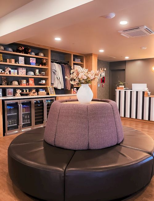 A chic lounge area with a round, cushioned seating pod in the center, wine racks and a bar on the left, and a striped reception desk on the right.