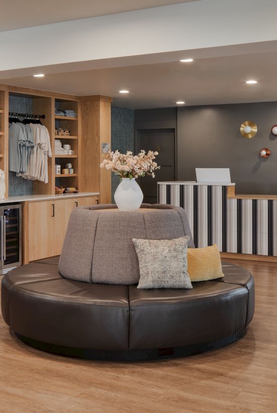 A modern reception lounge with a desk, bottle/wine display, flowers, and stylish wall decor in soft colors.