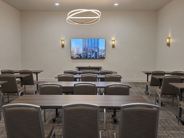 A modern conference or training room with a large screen at the front, rows of tables and chairs, soft lighting, and a clean, neutral decor.