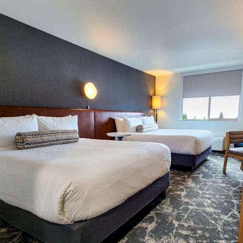 A modern hotel room with a large bed, beige walls, a desk, and a balcony view; warm lighting and a clean, contemporary design.