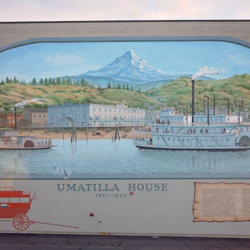 A wall mural shows a steamship flotilla on a river with mountains in the background, likely depicting the Umatilla House.