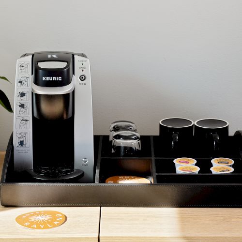 A Keurig coffee maker sits on a countertop with a drip tray, carafe, and coffee pods, ready to brew.