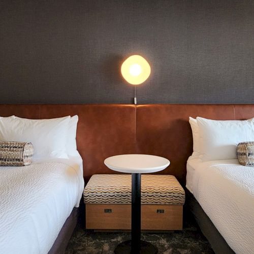 A neatly made hotel bed with fluffy pillows, soft lighting, and a cozy nightstand in a modern, minimalist room.