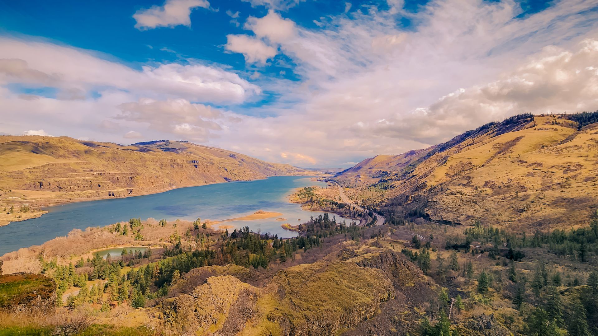 The image shows a river flowing through a rocky, mountainous landscape under a blue sky with clouds.