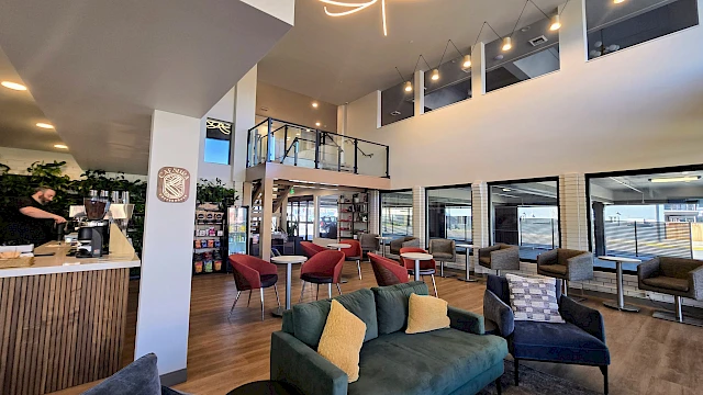 A stylish hotel lobby with a green sofa, red chairs, multiple lounge areas, large windows, and a staircase to an upper level, bright and inviting.